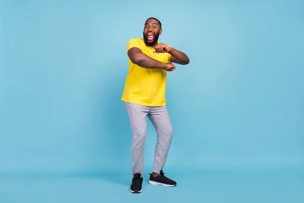 Bilde av den sjokkerte, mørkhudede mannen med gul T-skjorte danser smilende, blå fargebakgrunn – stockfoto