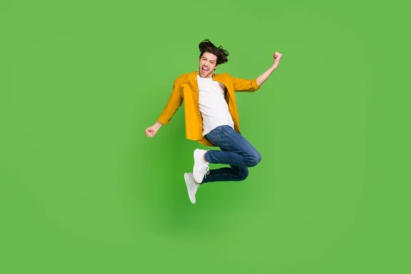 Photo of attractive lucky young man wear yellow shirt smiling jumping rising fists isolated green color background — Stock Photo, Image