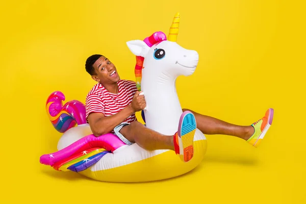 Foto de cuerpo completo de chico nadar unicornio boya salvavidas océano llevar ropa de rayas rojas aisladas sobre fondo de color amarillo brillante — Foto de Stock