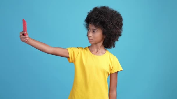 Lockigt hår bloggare kid gör enheten selfie v tecken isolerad blå färg bakgrund — Stockvideo