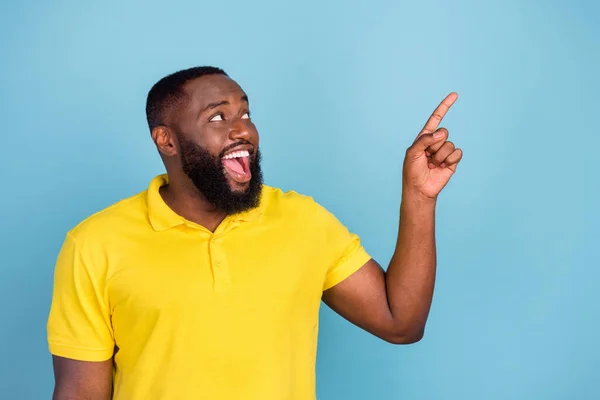 Photo of pretty shocked dark skin man wear yellow t-shirt smiling pointing finger looking empty space isolated blue color background — Stock Photo, Image