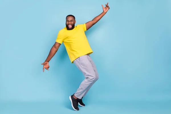 Fénykép izgatott vicces sötét bőrű fickó öltözött sárga póló tánc mosolygós elszigetelt kék szín háttér — Stock Fotó