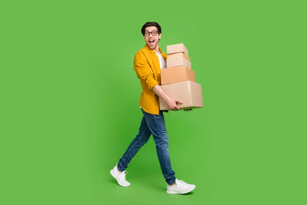 Foto ukuran penuh dari pemuda tampan bersuasana hati yang baik pergi berjalan sambil memegang kotak karton memindahkan rumah baru yang terisolasi dengan latar belakang warna hijau — Stok Foto