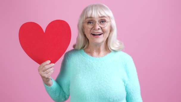 Viejo abuelita hold tarjeta corazón presente puño hasta aislado pastel color fondo — Vídeo de stock