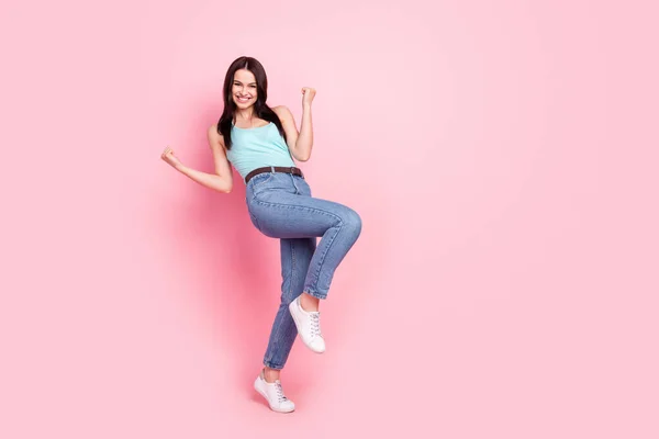 全身写真のお祝い千年の女性の手拳はピンクの背景に隔離された青いトップジーンズスニーカーを身に着けている — ストック写真