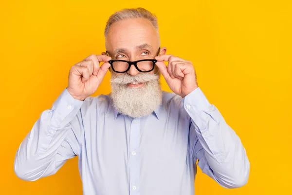 Foto de barba alegre homem envelhecido olhar espaço vazio desgaste óculos camisa azul isolado no fundo cor amarela — Fotografia de Stock