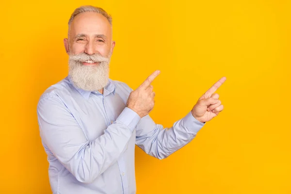 自信を持って魅力的な年齢の紳士の写真は、 2本の指を指して青いシャツを着用空のスペース孤立黄色の背景 — ストック写真