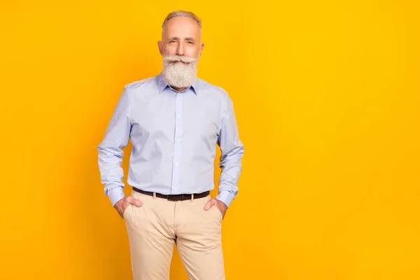 Photo of confident attractive age gentleman wear blue shirt standing arms pockets empty space isolated yellow color background — Stock Photo, Image