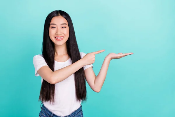Фото молодой азиатской девушки счастливая положительная улыбка указывает пальца промо продукт предложение изолированы на бирюзовом фоне цвета — стоковое фото