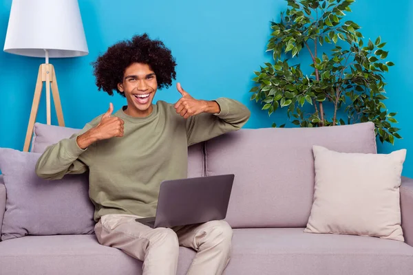 Fotografie mladého vzrušený chlap sedět divan show thumb-up feedback select use laptop isolated over blue color background — Stock fotografie