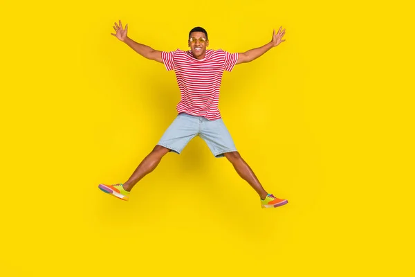 Plná délka fotografie mladého člověka skok držet ruce stranou nosit červené pruhované oblečení izolované přes jasně žluté barvy pozadí — Stock fotografie