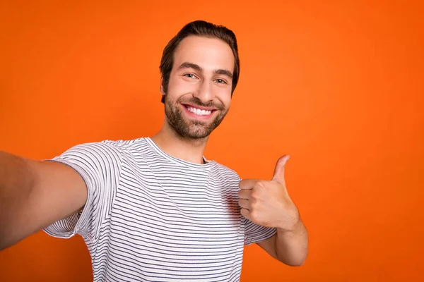 Zdjęcie młody wesoły facet pokazać palec reklamy wybrać podjąć selfie wideo połączenie izolowane ponad pomarańczowy kolor tła — Zdjęcie stockowe