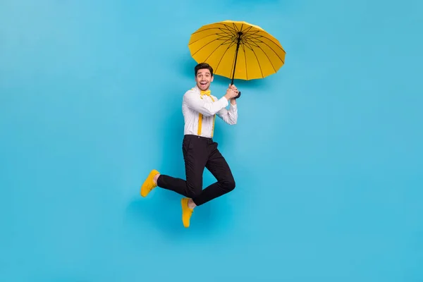 Foto de corpo inteiro de animada pessoa satisfeita segurar guarda-chuva mosca isolada no fundo de cor azul — Fotografia de Stock