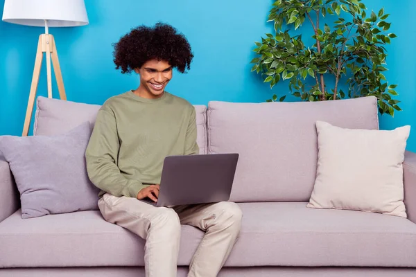 Fotografie mladého muže sedět divan použít notebook typ chatování digitální moderní izolované přes modré barvy pozadí — Stock fotografie