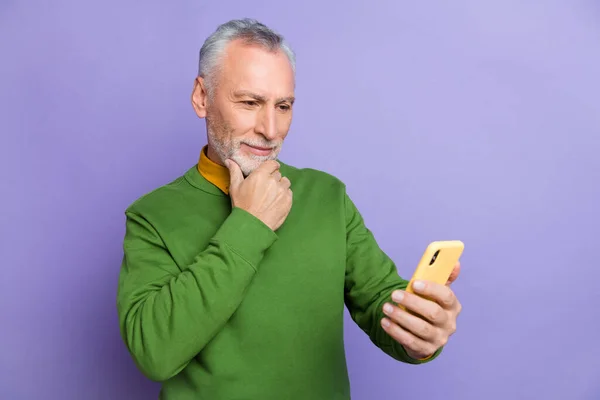 Photo of thoughtful retired man wear green sweater typing modern device isolated violet color background — Stock Photo, Image