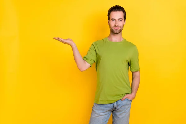 Foto de la barba optimista joven sostiene espacio vacío desgaste camiseta vaqueros aislados sobre fondo de color amarillo —  Fotos de Stock