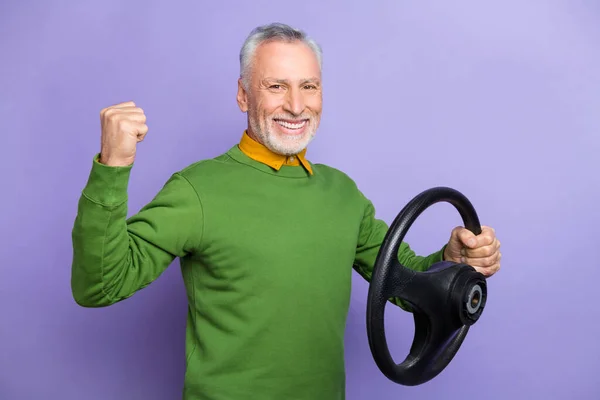 Foto von lustigen glücklichen Rentner tragen grünen Pullover Reiten Auto steigende Faust isoliert violette Farbe Hintergrund — Stockfoto