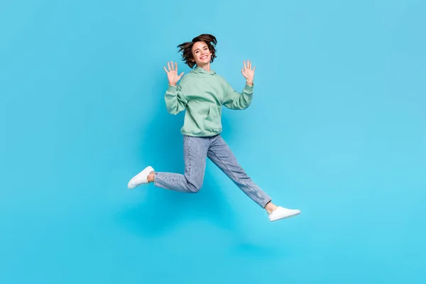 Full length foto di impressionato millennial bruna signora salto onda usura pullover jeans scarpe da ginnastica isolato su sfondo blu — Foto Stock