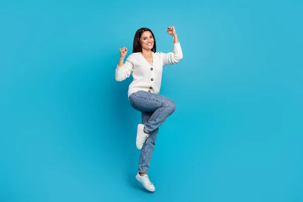 Foto de mujer dulce afortunada usar cárdigan blanco saltando puños de gran altura aislado fondo de color azul —  Fotos de Stock