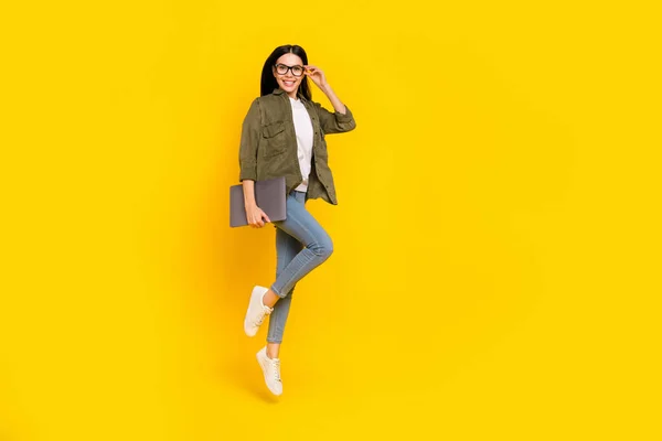 Teljes méretű fotó vicces fiatal hölgy ugrás hold laptop visel szemüveg ing farmer lábbeli elszigetelt sárga háttér — Stock Fotó