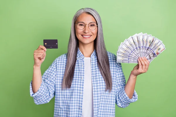 Foto van optimistisch oud wit kapsel dame houd kaart geld dragen bril geruite shirt geïsoleerd op groene kleur achtergrond — Stockfoto