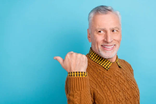 Photo of pretty funny retired man wear brown sweater pointing empty space isolated blue color background — Stock Photo, Image