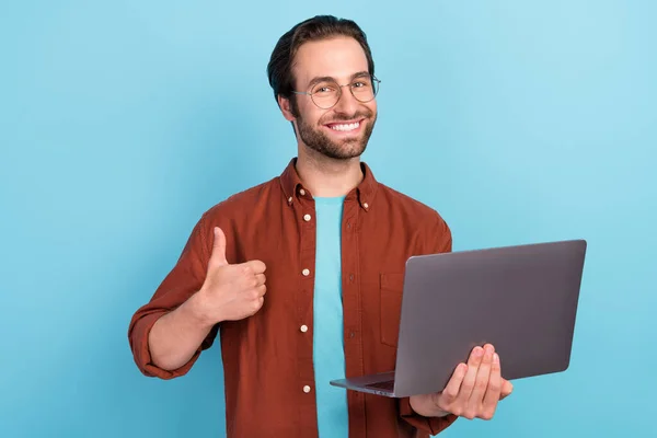 Фото головного брюнетки тисячоліття хлопець тримає ноутбук великий палець вгору одяг показує тенденцію вписуватися ізольовано на синьому кольоровому фоні — стокове фото
