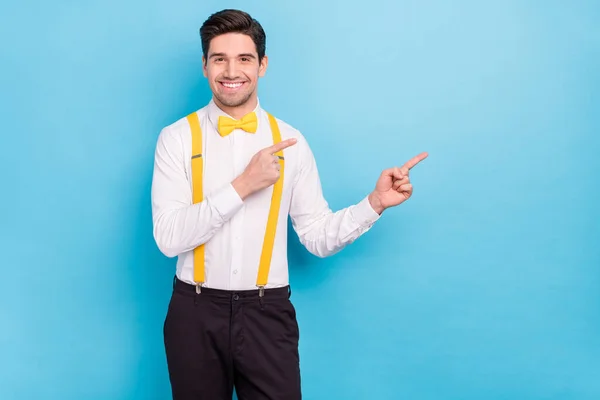 Foto de cara bonito encantador usar suspensórios amarelos camisa branca apontando espaço vazio isolado fundo cor azul — Fotografia de Stock