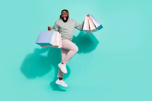 Повнометражний вигляд на тіло привабливого веселого модного хлопця, який стрибає, доставляючи подарунки ізольовані на яскравому фоні бірюзового кольору — стокове фото