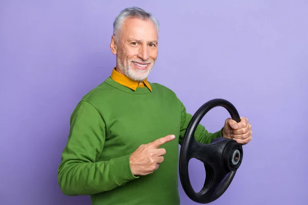 Photo of cheerful man pensioner dressed green pullover pointing steering wheel isolated purple color background — Stock Photo, Image
