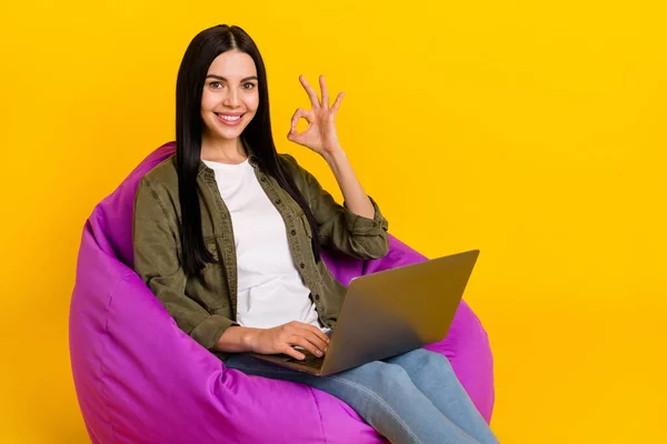 Foto wanita milenial lucu duduk tipe laptop menunjukkan okey mengenakan celana jeans kaus terisolasi di latar belakang kuning — Stok Foto