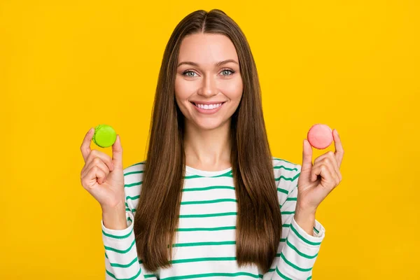 Φωτογραφία από γλυκό όμορφη κυρία ντυμένη ριγέ πουκάμισο επιλέγοντας πράσινο ροζ cookies απομονωμένο κίτρινο χρώμα φόντο — Φωτογραφία Αρχείου