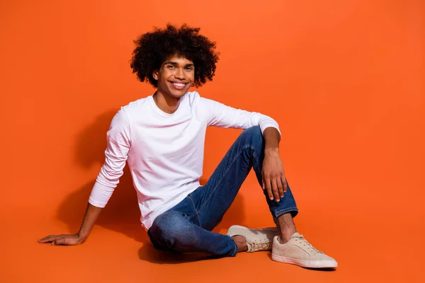 Foto de dulce lindo chico usar camisa blanca sonriendo sentado piso tener resto aislado de color naranja de fondo —  Fotos de Stock