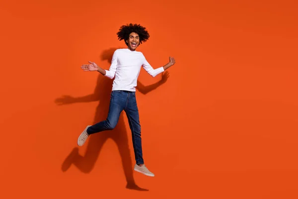 Foto de cara muito impressionado vestido camisa branca correndo rápido saltando alto espaço vazio isolado cor de fundo laranja — Fotografia de Stock