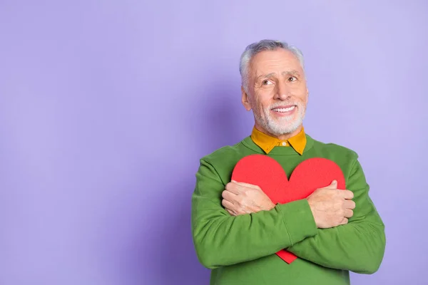 Photo de charmant homme pensionné habillé pullover vert étreignant grand coeur vide espace isolé couleur pourpre fond — Photo