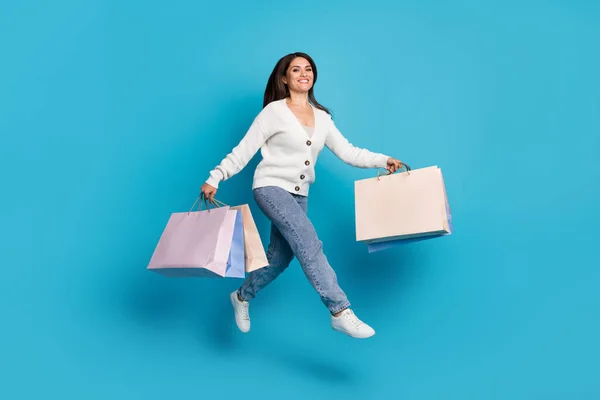 Foto de dulce linda dama vestida de cárdigan blanco llevando compradores corriendo rápido aislado fondo de color azul —  Fotos de Stock