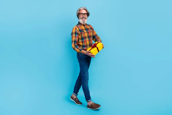 Foto de divertido hombre jubilado excitado usar gafas de camisa a cuadros caminando sosteniendo presente caja aislado color azul fondo —  Fotos de Stock