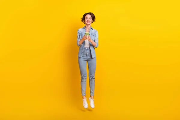 ( 영어 ) Full body photo of young girl use mobile jump subscribe repost share app jump isolated over yellow color background — 스톡 사진