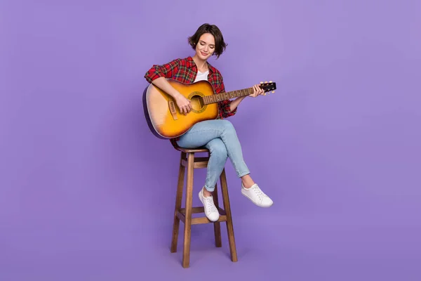 Volledige lengte foto van mooie millennial brunette dame spelen gitaar slijtage shirt jeans sneakers geïsoleerd op paarse kleur achtergrond — Stockfoto