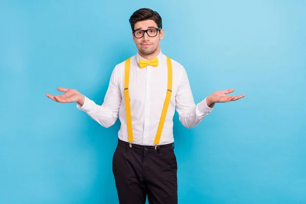 Çekici, kafası karışık bir adamın fotoğrafı sarı pantolon askısı takıyor beyaz gömlek gözlük omuzlarını silkiyor mavi arka plan. — Stok fotoğraf