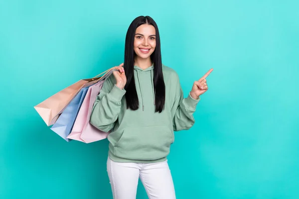 Fotografie krásné Millennial brunetka lady index promo držet tašky nosit zelený svetr izolované na pozadí teal barva — Stock fotografie