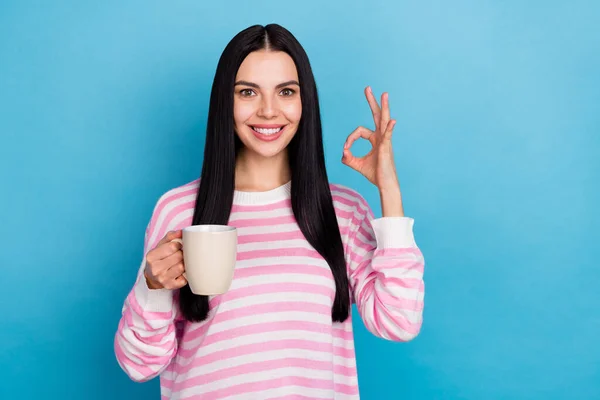 Fotografie mladé krásné dámy pít latte cacao show prsty okey symbol doporučit perfektní izolované přes modré barvy pozadí — Stock fotografie