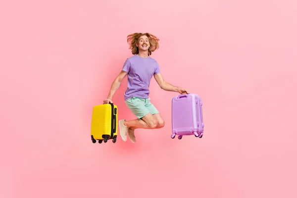 Ganzkörpergröße Ansicht der attraktiven fröhlichen Kerl springen Haltekoffer Low-Cost-Flug isoliert über rosa Pastellfarbe Hintergrund — Stockfoto