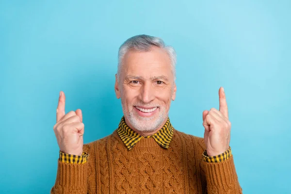 Foto de dulce hombre alegre pensionista vestido jersey marrón señalando espacio vacío aislado color azul fondo — Foto de Stock