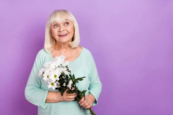 Foto de excitado aposentado senhora segurar presente flores monte olhar vazio espaço desgaste teal camisa isolado violeta cor fundo — Fotografia de Stock
