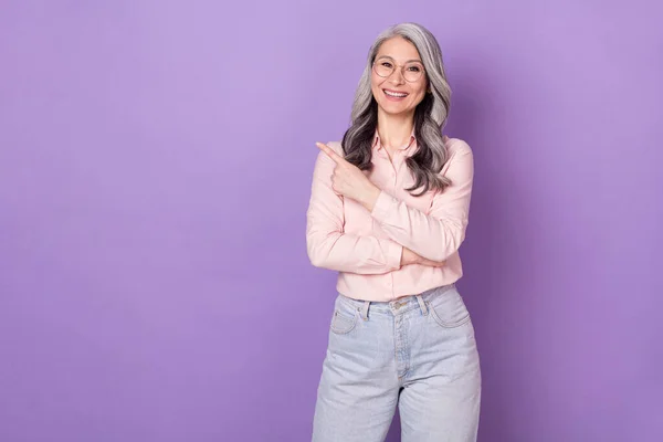 Portret van aantrekkelijke trendy bejaarde gepensioneerde vrolijke zakenvrouw demonstreren kopieerruimte ad geïsoleerd over violet paarse kleur achtergrond — Stockfoto