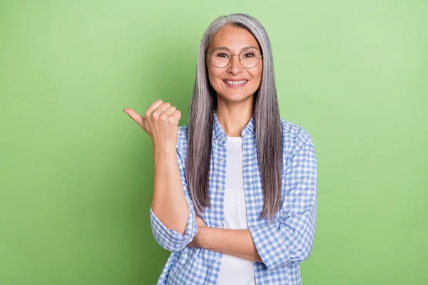 Foto de señora lindo peinado blanco envejecido indican promo desgaste gafas camisa a cuadros aislado sobre fondo de color verde — Foto de Stock