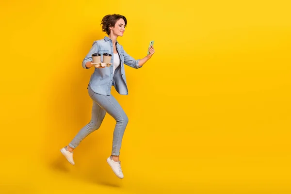 フルボディプロフィールサイド写真の若いです女の子ジャンプホールドモバイルランカプチーノブレーク絶縁上の黄色の色の背景 — ストック写真