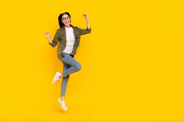 젊은 숙녀가 점프하는 것을 기념하는 사진의 전체 사이즈는 노란 배경에 고립된 아이피 셔츠 청바지 운동화를 신고 있다 — 스톡 사진