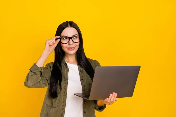 Fénykép csinos fiatal hölgy hold laptop megjelenés hirdetés kopás szemüveg khaki ing elszigetelt sárga háttér — Stock Fotó